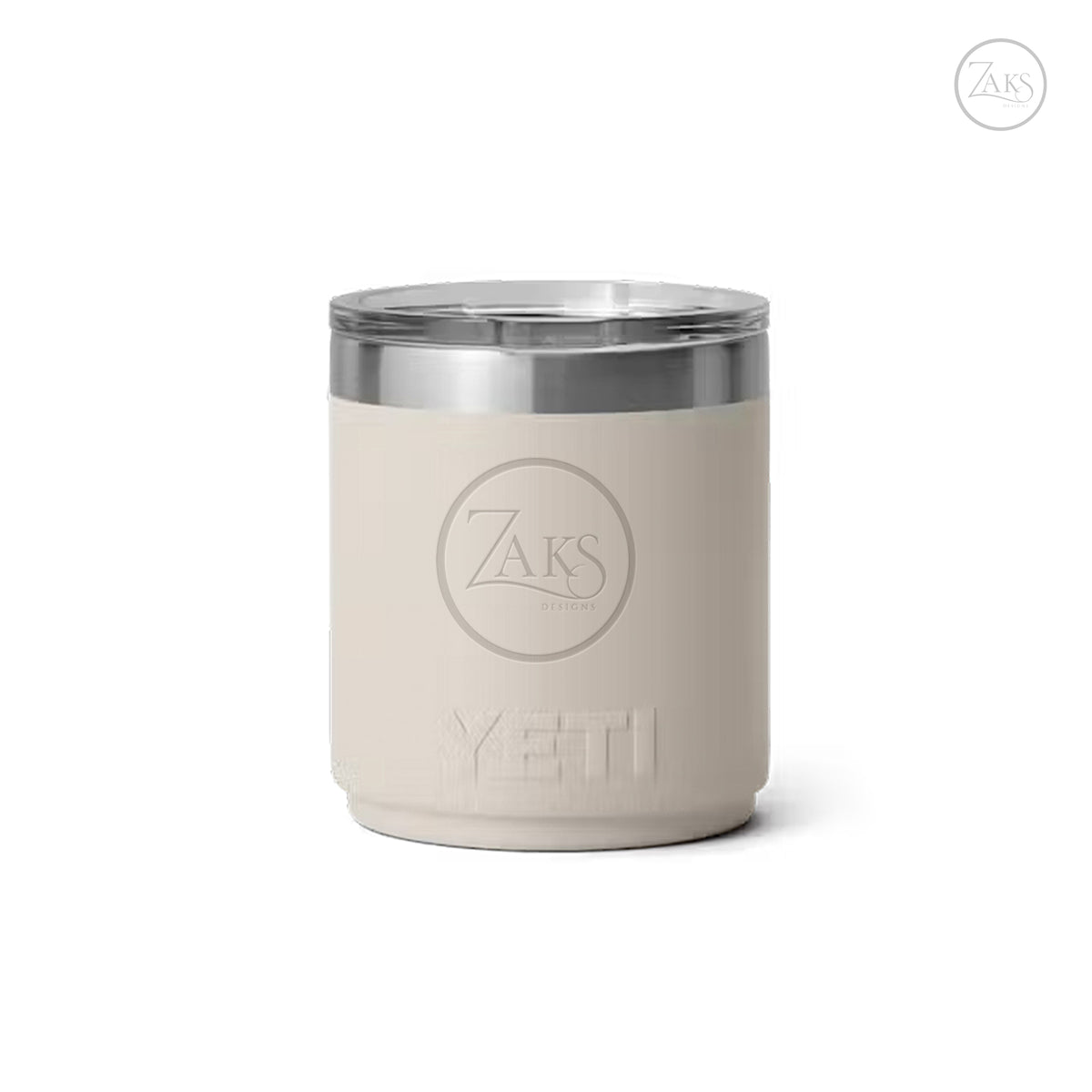 A beige YETI insulated tumbler with a clear lid and a silver metal rim, featuring an embossed ZAKS logo on the front, set against a plain white background.