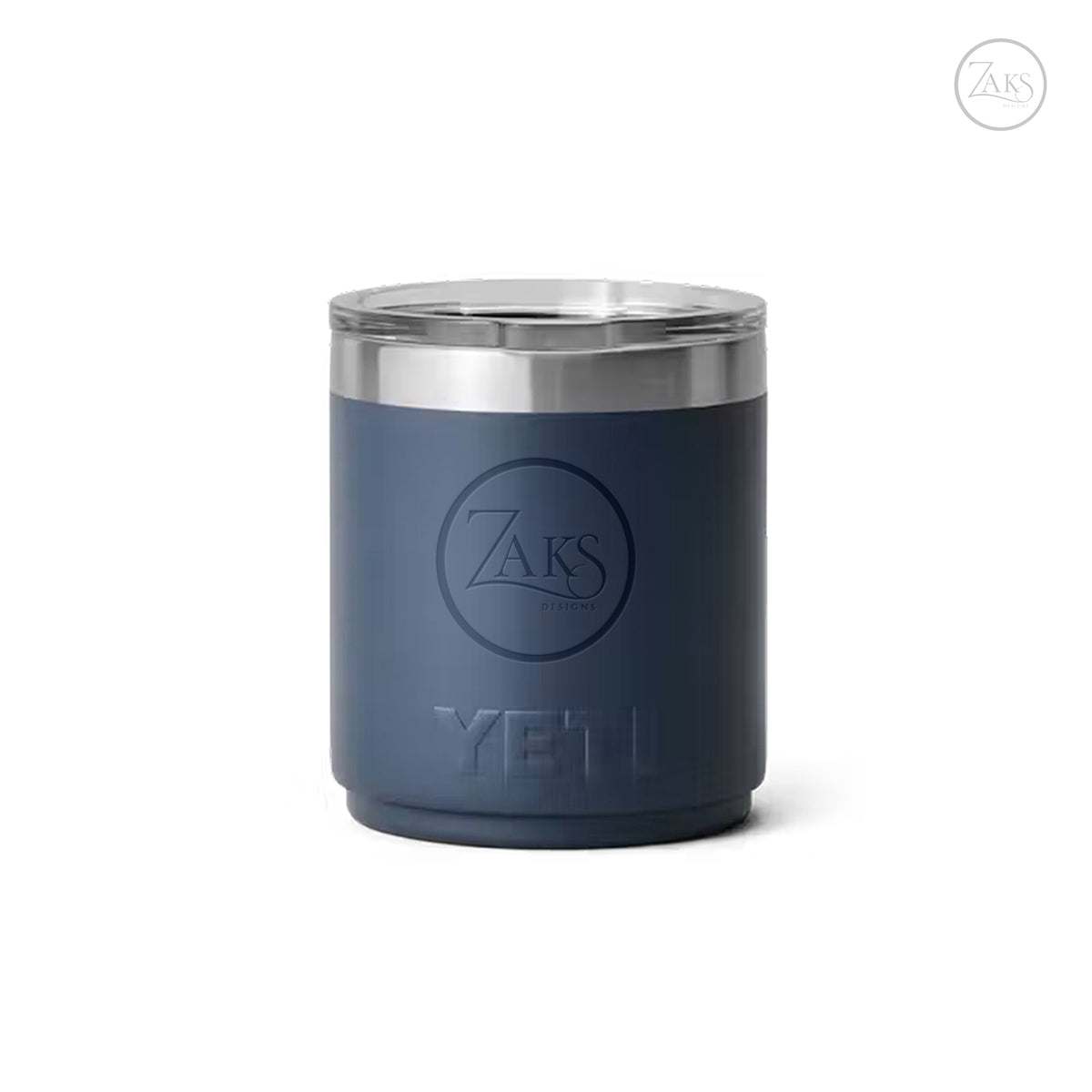 A dark slate blue YETI insulated tumbler with a stainless steel rim and a clear lid, featuring an embossed circular ZAKS logo and the word YETI on the front, set against a plain white background.